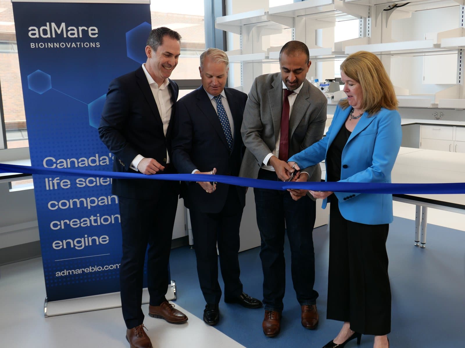 Four people cutting a blue ribbon in a new laboratory beside an adMare BioInnovations banner